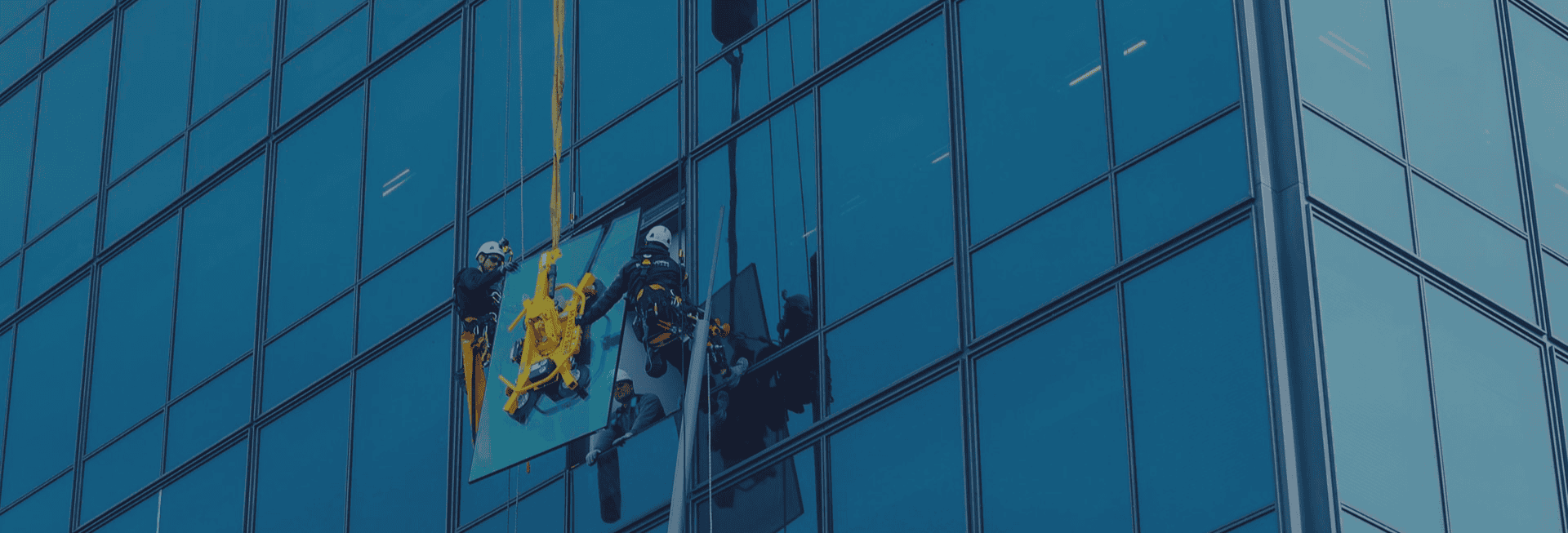 Polished blue glass storefront windows on modern building with glaziers installing large glass panels in Vancouver, BC, for commercial glass solutions.
